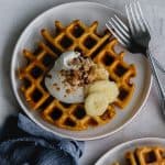 pumpkin waffle on a plate with whipped cream, bananas, pecans and pumpkin pie spice