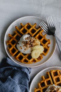 pumpkin waffle on a plate with whipped cream, bananas, pecans and pumpkin pie spice