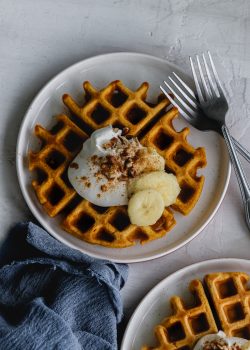 pumpkin waffle on a plate with whipped cream, bananas, pecans and pumpkin pie spice
