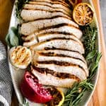 slices of turkey decoratively displayed on an oval serving tray with a garlic head, charred lemon and fresh sage, thyme and rosemary.