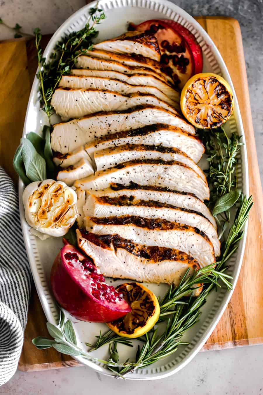 slices of turkey decoratively displayed on an oval serving tray with a garlic head, charred lemon and fresh sage, thyme and rosemary.