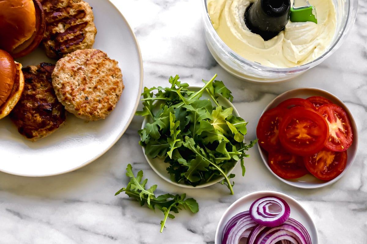 ingredients for the burgers: turkey patties, brioche bun, arugula, tomatoes and red onion. With the food processor of whipped feta spread.