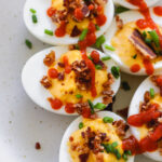 sriracha deviled eggs with bacon on a white plate