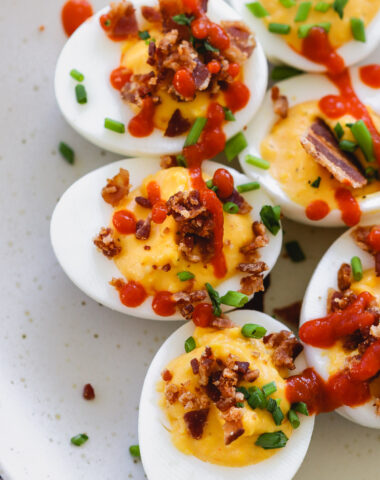 sriracha deviled eggs with bacon on a white plate