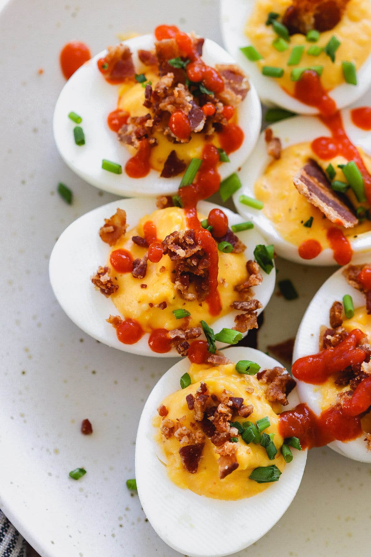 sriracha deviled eggs with bacon on a white plate