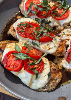 A pan with chicken, mozzarella tomatoes and basil.